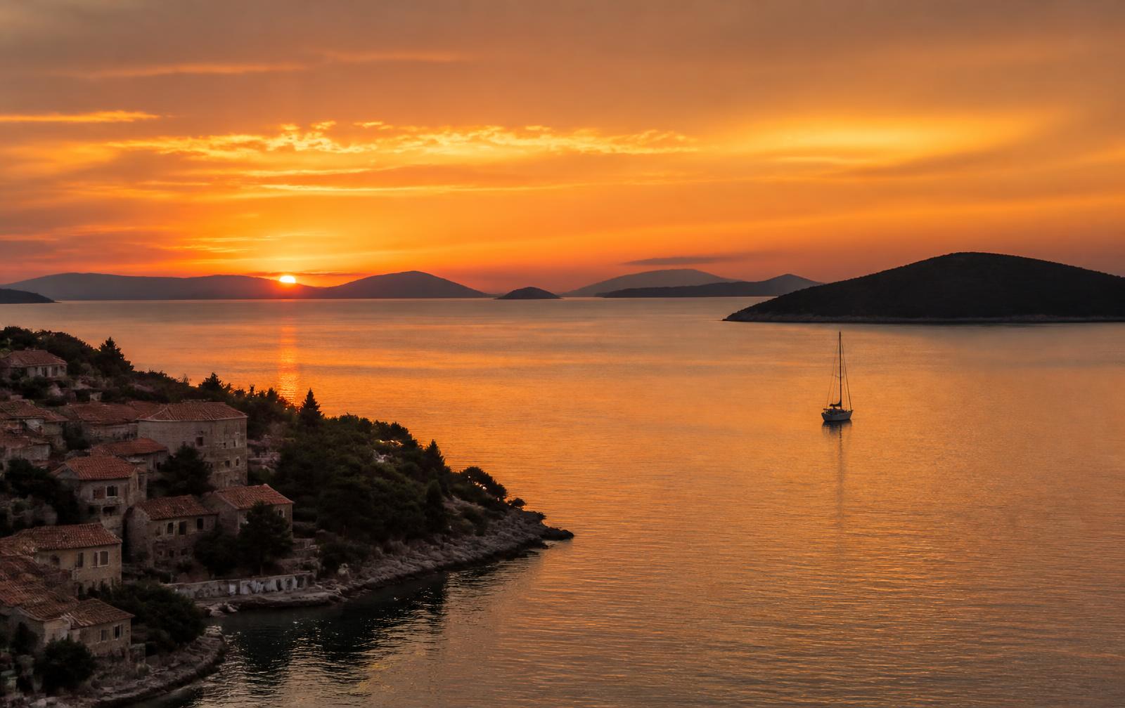 Sunset over the Dalmatian coast with islands, a sailboat and a stone village